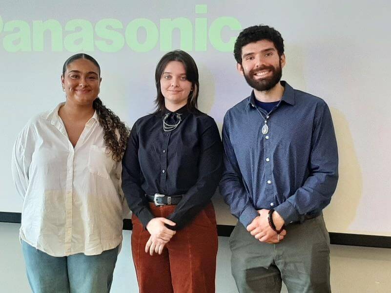 Three students posing for photo in front of a projector screen