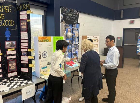 Two sthree students and teacher near poster presentations