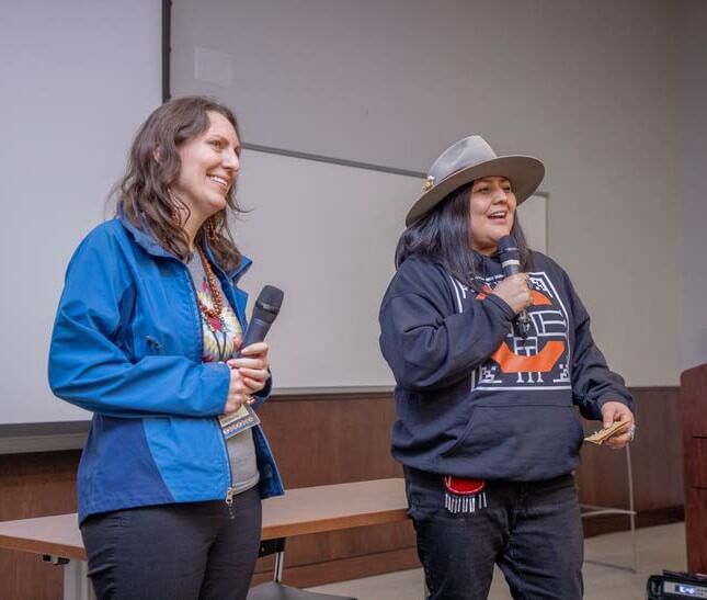 Two women with microphones smiling, one in western hat speaking into the mic.