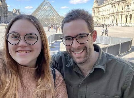 Woman and man taking selfie in front of that glass pyramid in front of the Louvre.