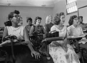 black and white photo from the mid 1900s showing black and white students in a classroom together.