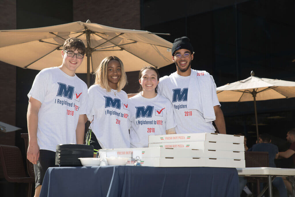 Students wearing shirts with the Monmouth University spirit logo, with text reading "I registered to Vote, 2018"