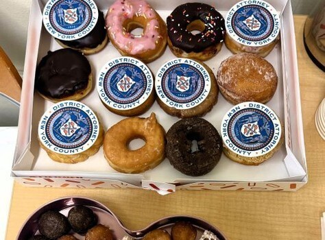 Table full of donuts, some of which have District Attorney New York County emblems on top.