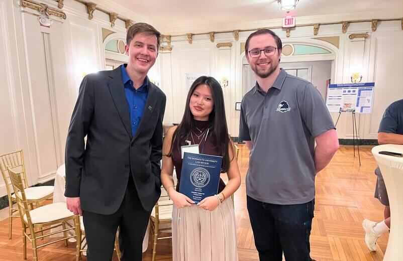 Woman holding bound thesis, with two men beside her
