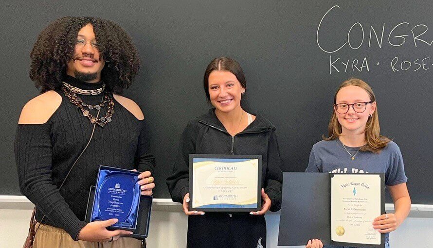 Three award winners holding their awards (one plaque, two certificates)