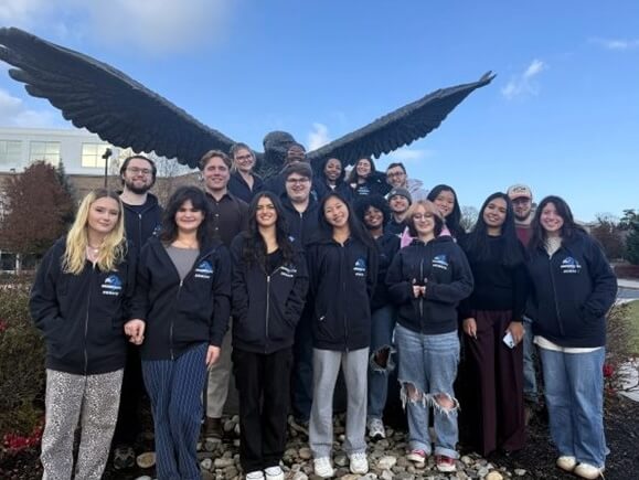 Students posing for photo under Hawk statue