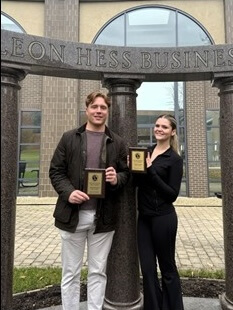 Two students holding award under Business School columns