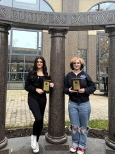 Two students holding award under Business School columns