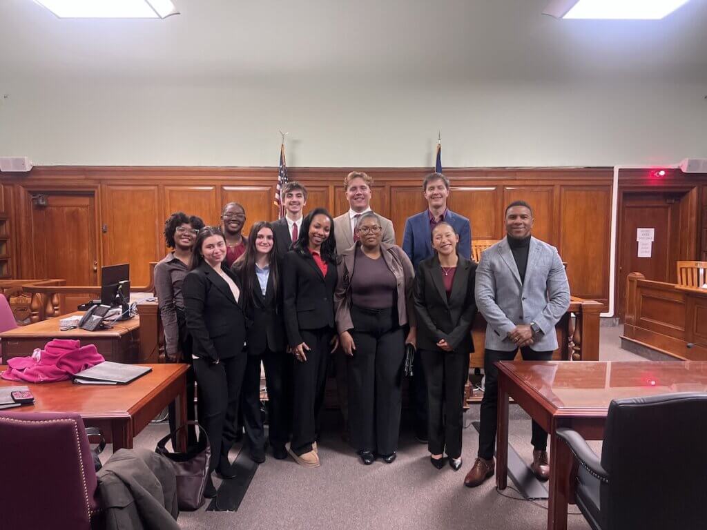Students in suits standing toward the front of a court-room like setting