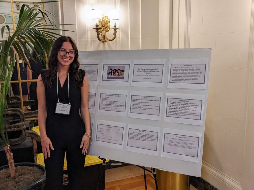 Student poses in front of her poster describing her psychology research.
  