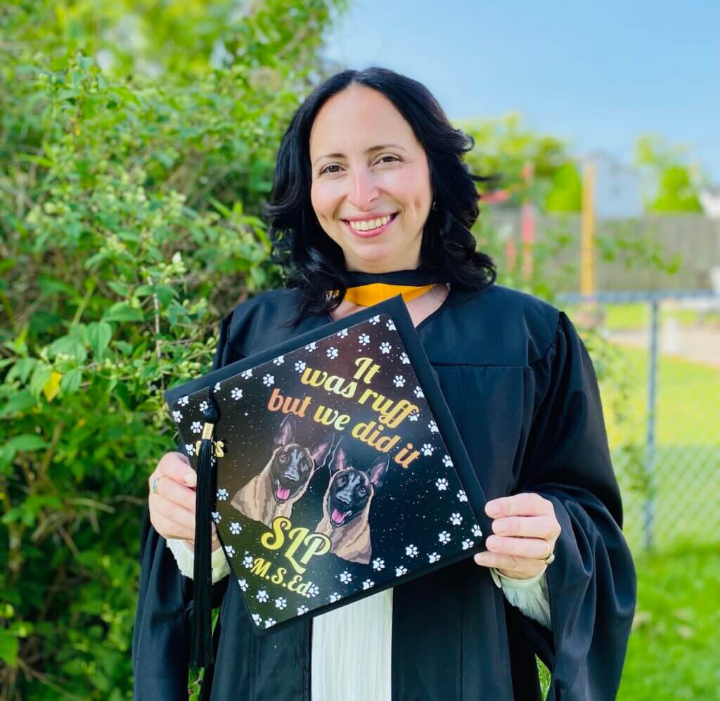 Ella Vardi Zamir in cap and gown. Cap features a drawing of two German shepherds, with a caption reading "It was ruff but we did it. SLP, MS.Ed.