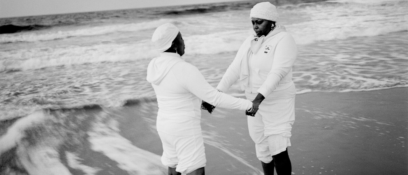 Andrew Lichtenstein photograph of two beachgoers holding each other's hands near a calm surf