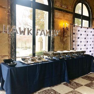 The words Hawk Family spelt in balloons shaped like letters hanging above table with catered food.