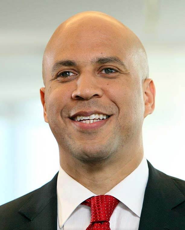 a headshot of Senator Cory Booker, who is wearing a black suit with a white shirt and red tie