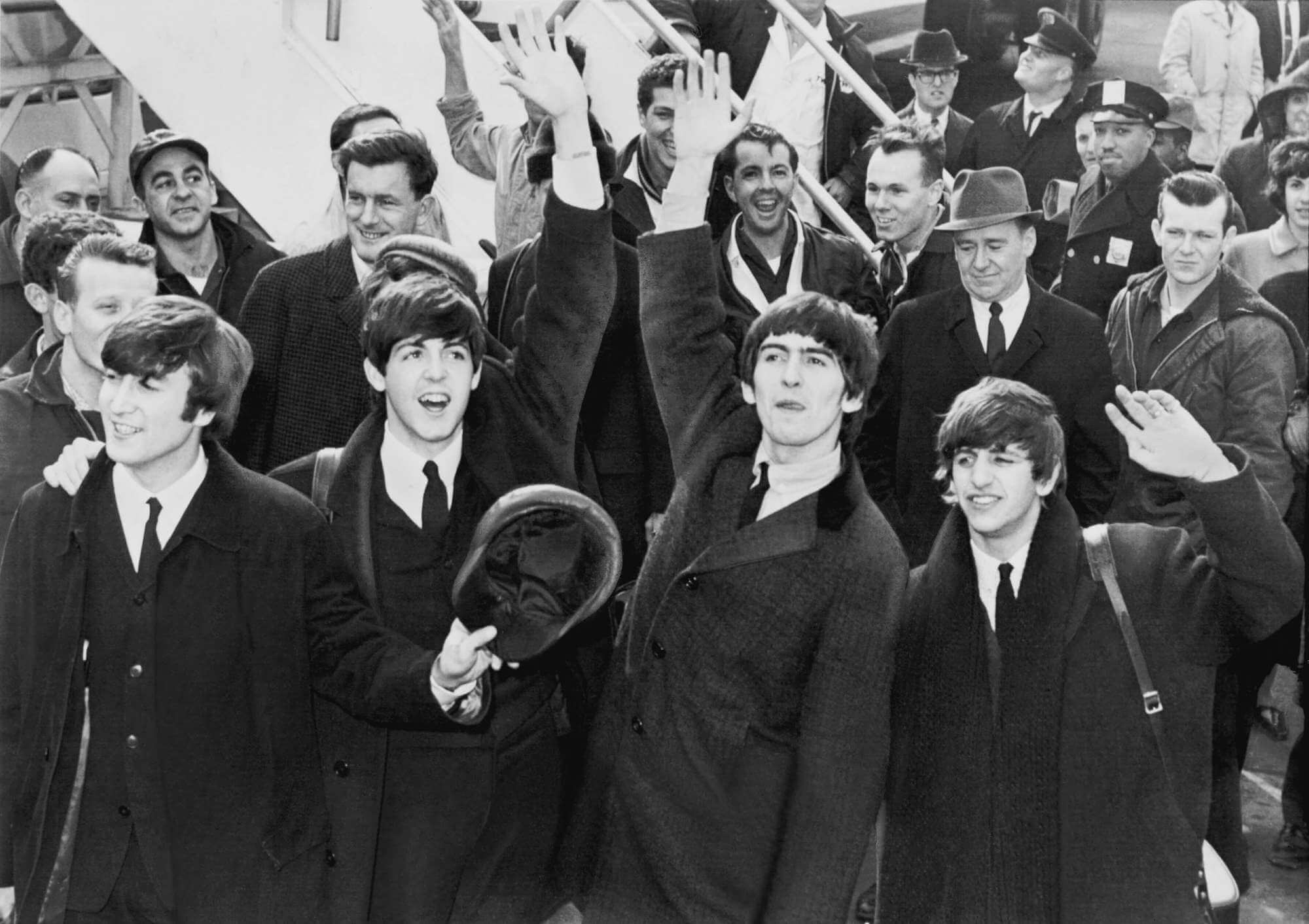 The Beatles waving their hands as police and onlokers smile in the background