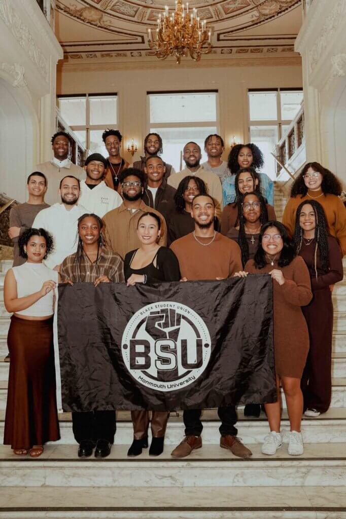 Group of twenty people standing on marble staircase, holding a flag that reads "BSU" with a black fist raised proudly behind the letters