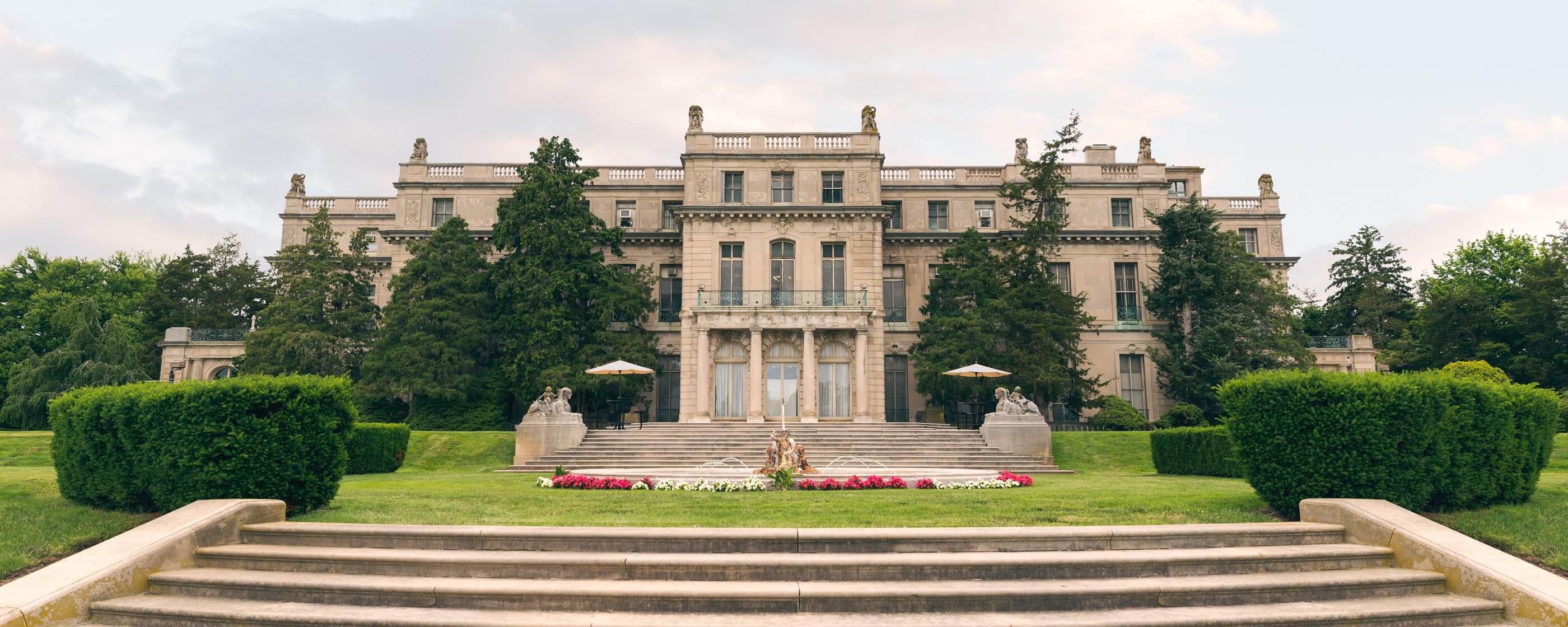 A photo of the Great Hall, a large mansion with a circular fountain in front of it.