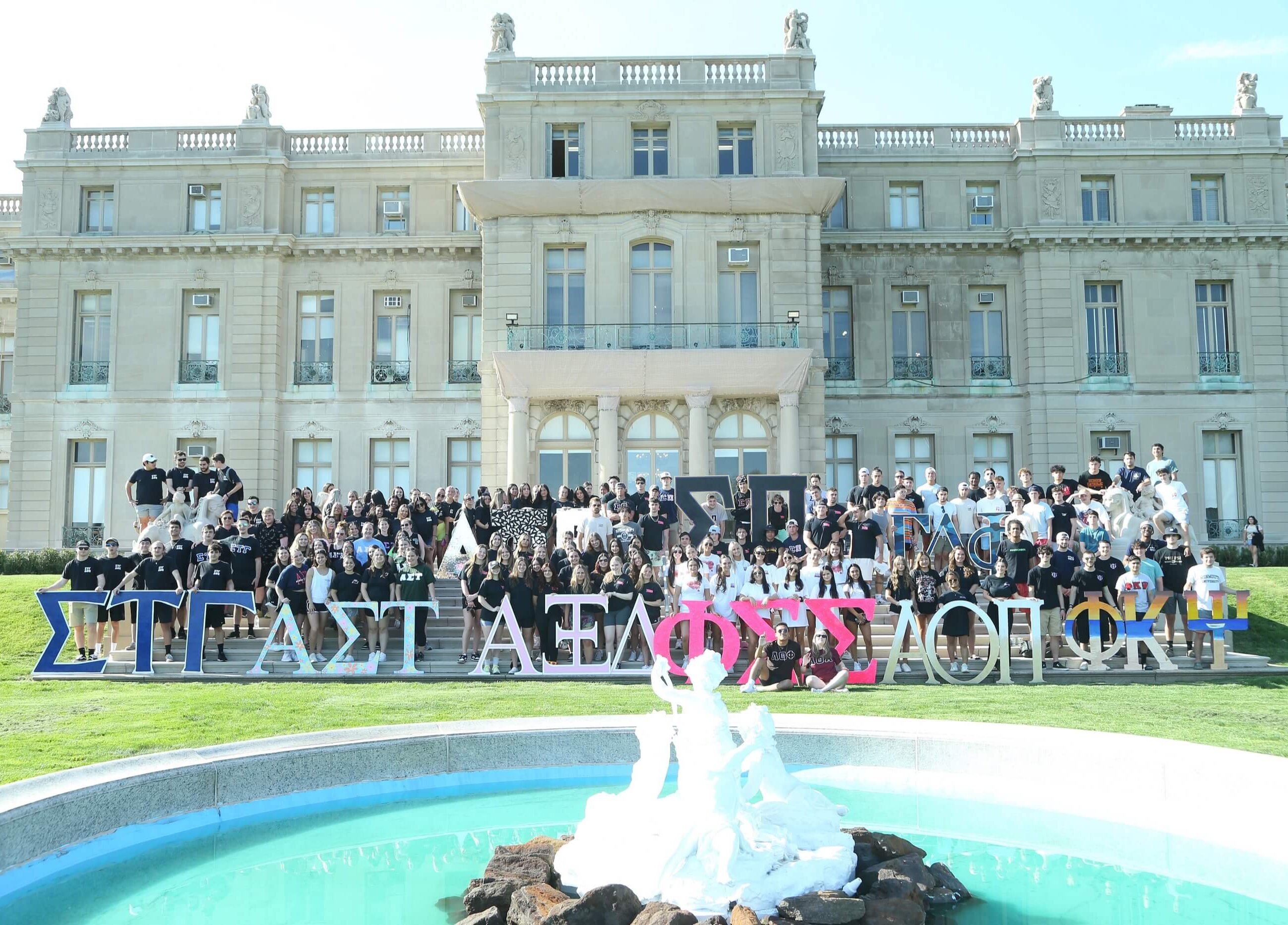 A large group of students representing different chapters of Greek life posing in front of the Great Hall.