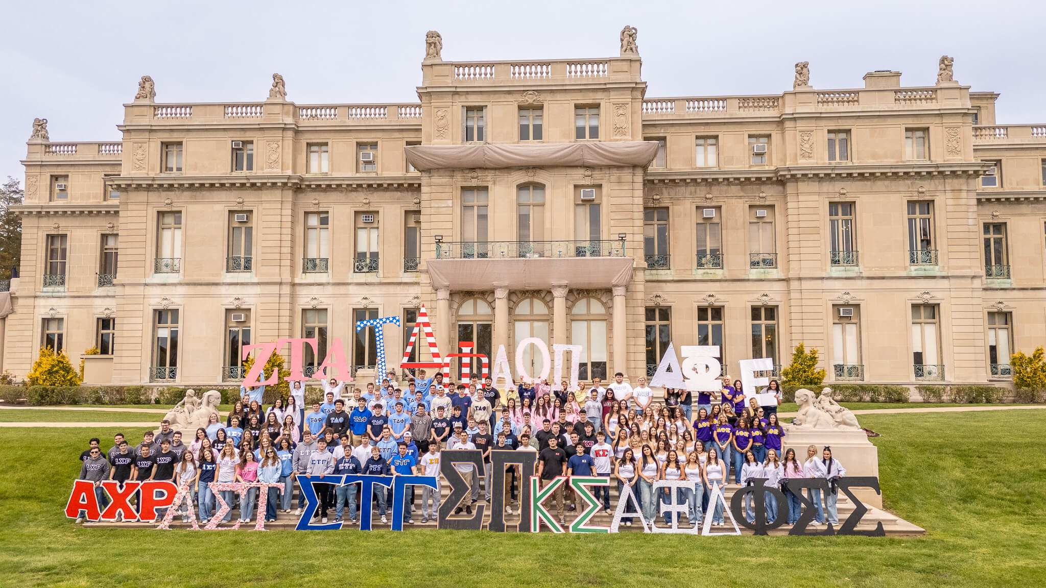 A large group of students representing different chapters of Greek life posing in front of the Great Hall.