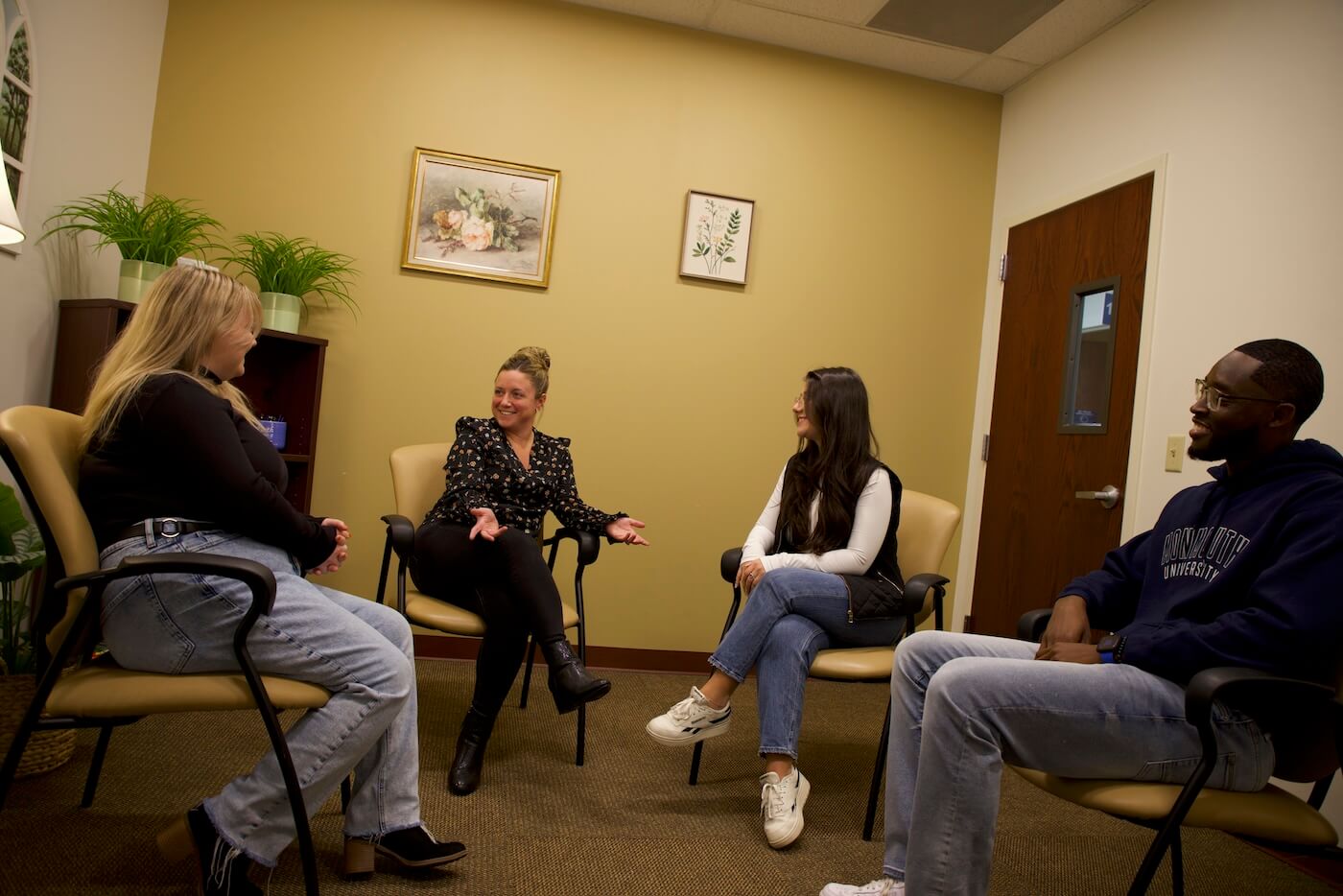 Four young adults sitting in the four corners of an office, speaking with one another.