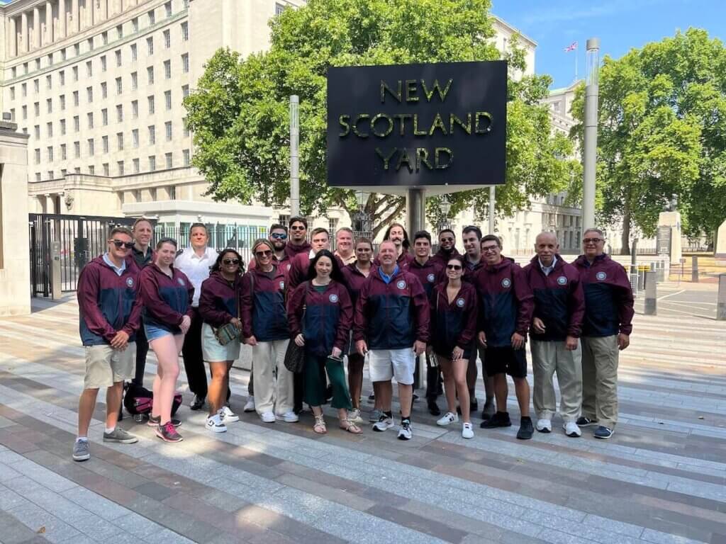 Group of around 20 men and women standing outside New Scotland Yard.