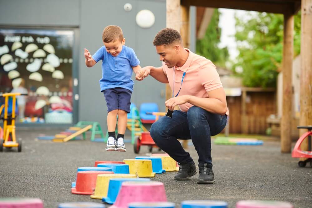 A child is jumping down a path of bright multicolored elevated risers while holding the hand of an instructor