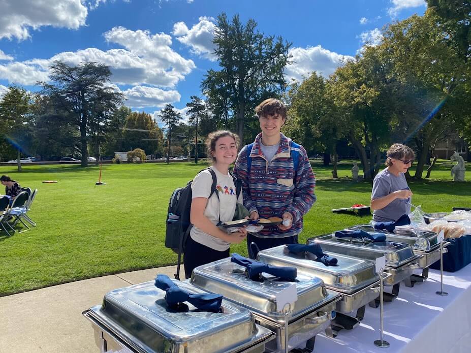 Students getting food from a buffet line outside on a green lawn