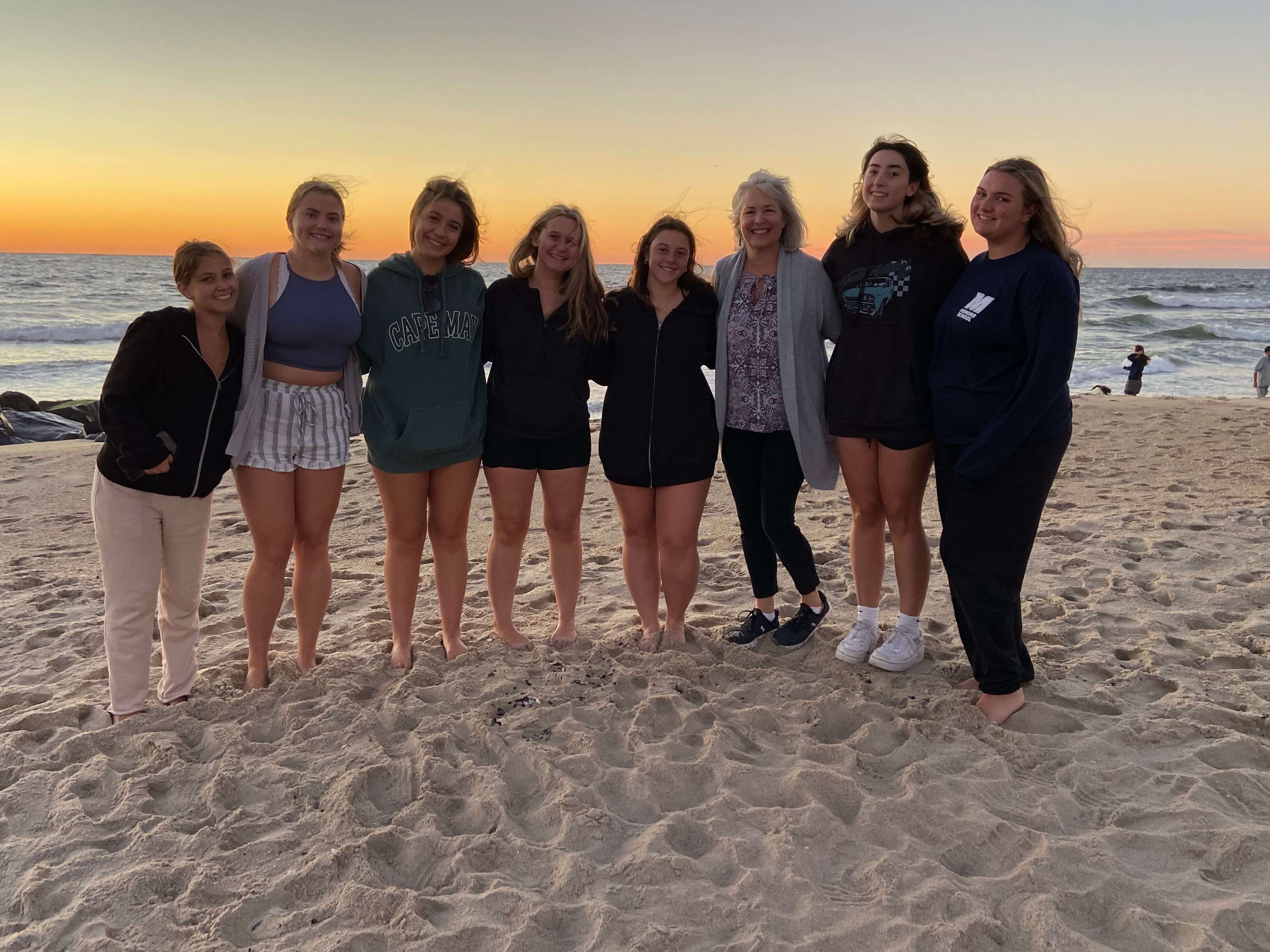 a group of students standing on the beach with the ocean behind them