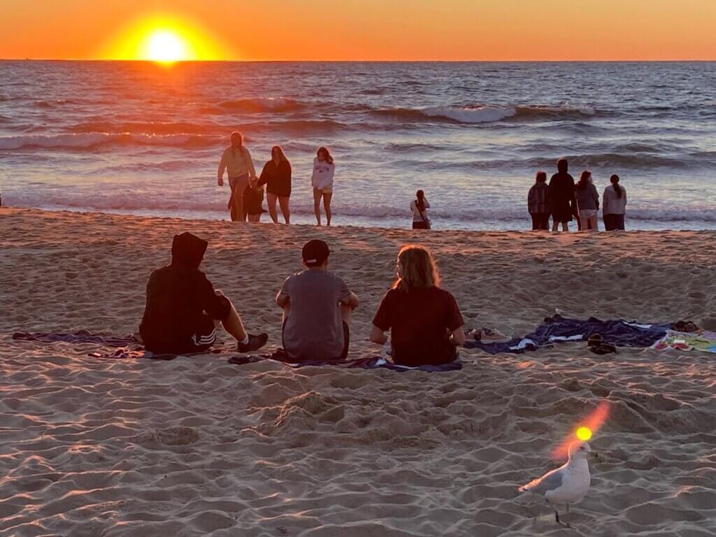 Students on the beach are looking out at the sun as it rises over the ocean