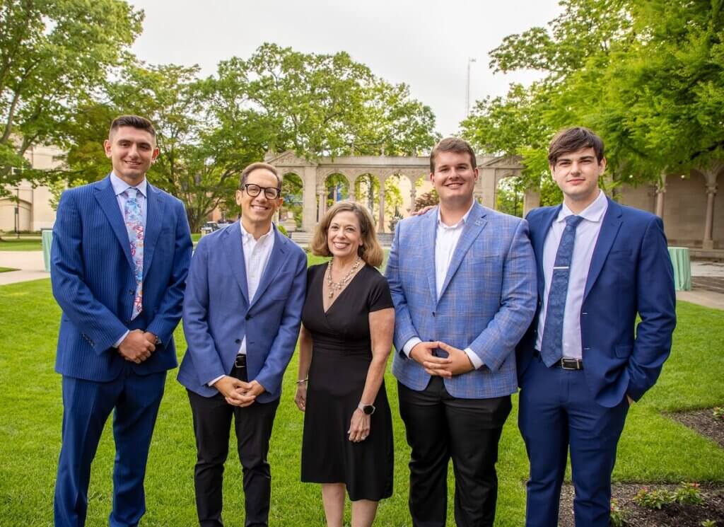 Four men and a women in suits, smiling for a photo in front of a large garden