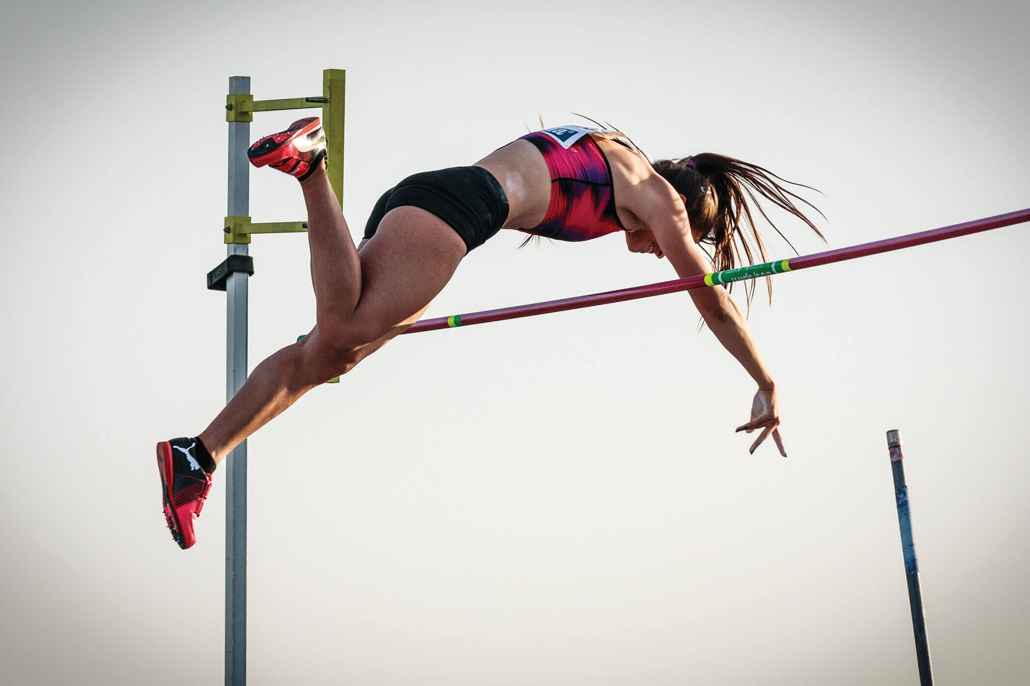 A mid-air pole vaulter arched over the bar she surmounted.