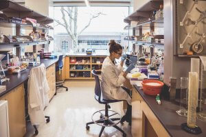 A researcher in a lab coat dropping chemicals into a beaker