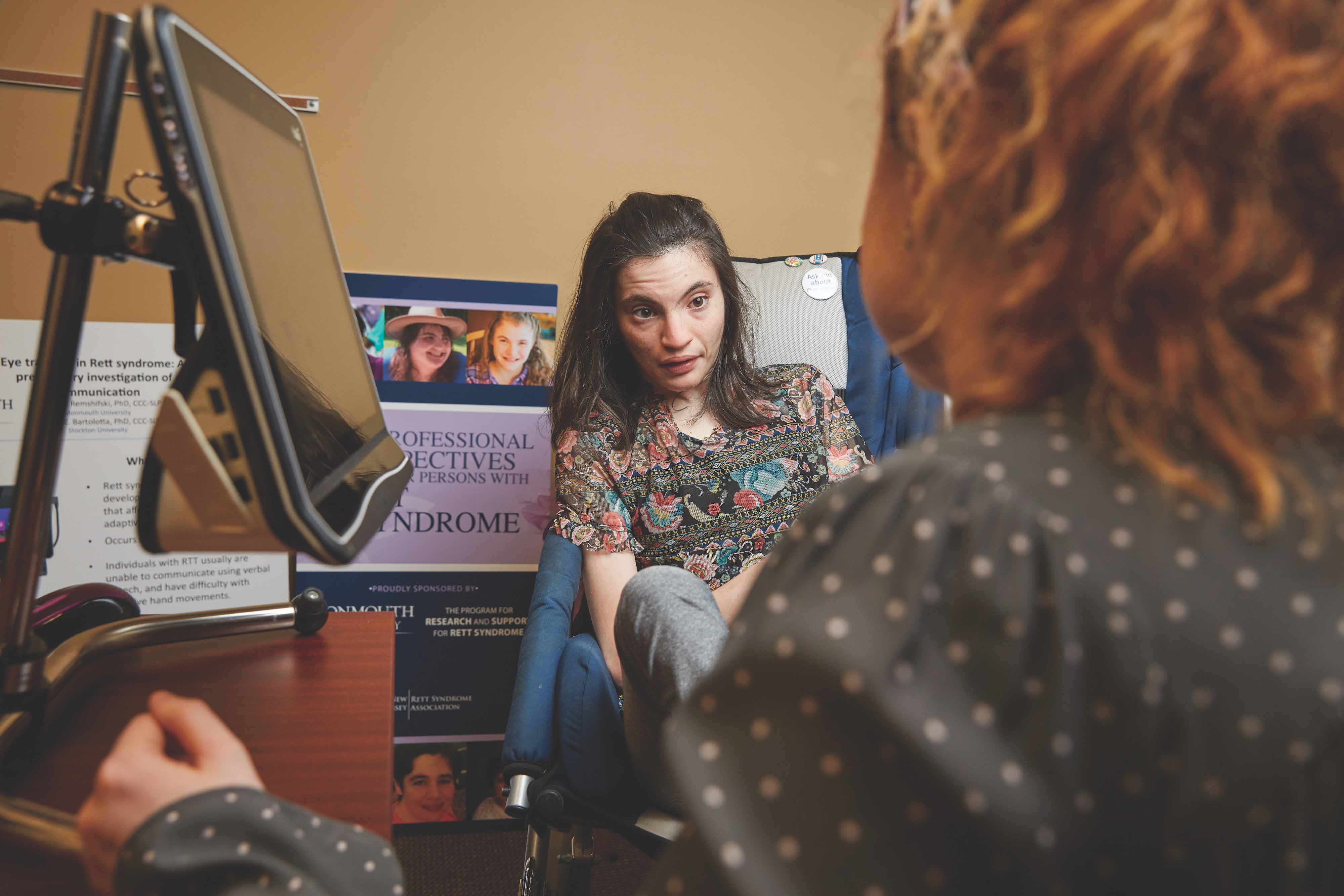 Graduate student Madison Chase (foreground) works with Michelle Saydah on improving her communications abilities when utilizing her eye-gaze equipment.