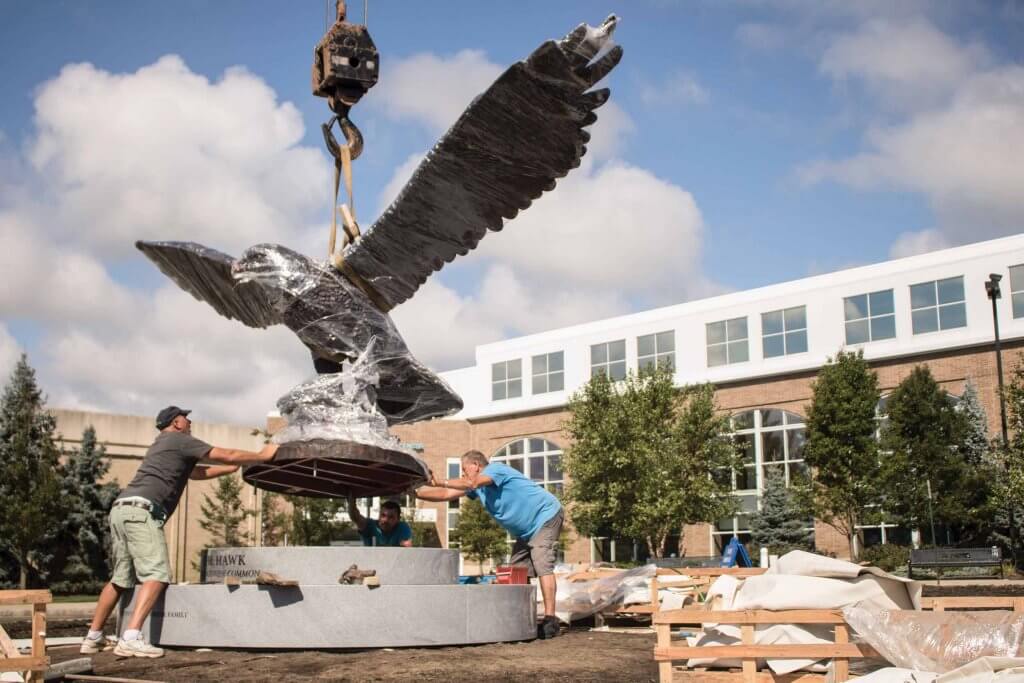 The Hawk at Brockriede Common suspended by a crane, with three workers manuevering the sculpture onto its podium