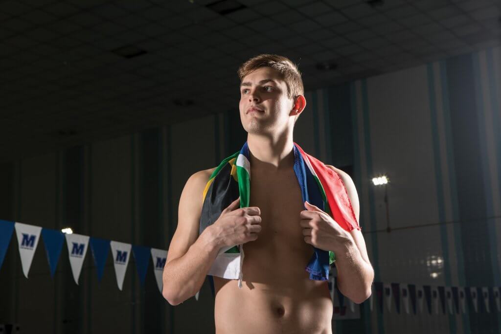 Dylan Barkhuizen standing in Richard E. Steadman Natatorium,adorned with the South African flag around his shoulders