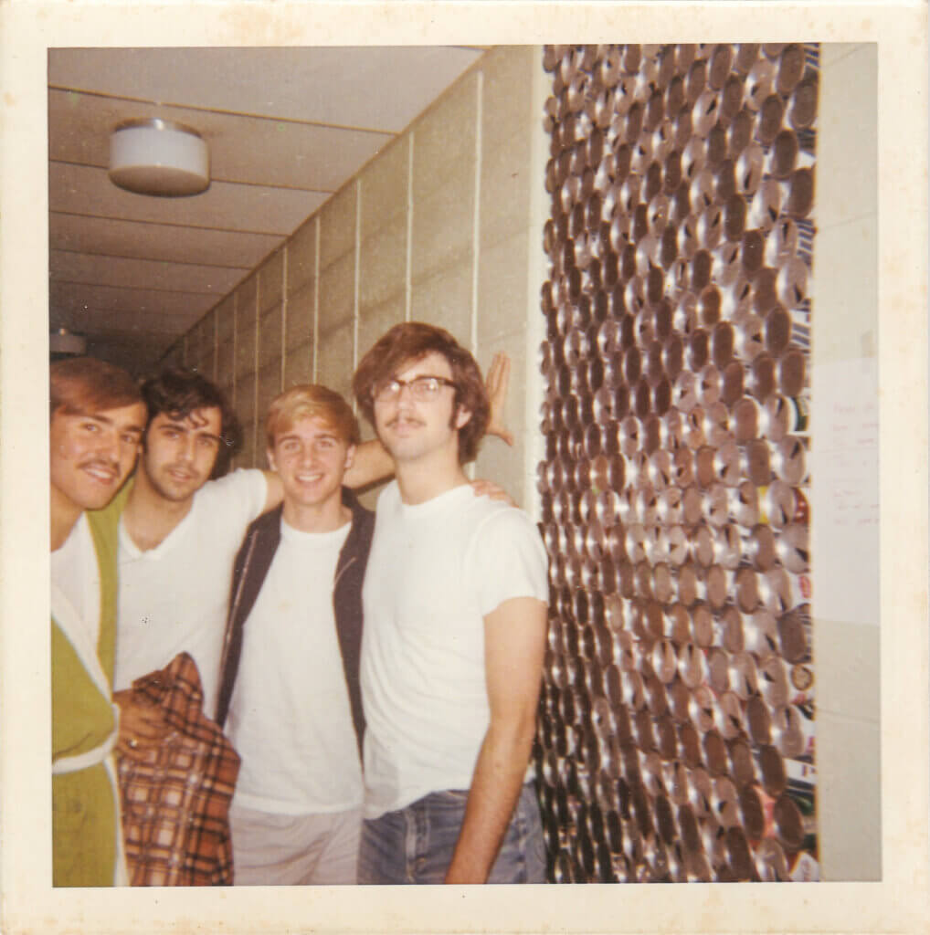 Four students from the 1970s pose outside a dorm room.