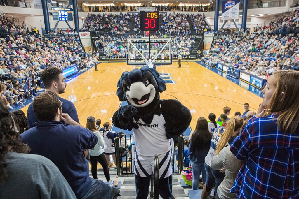 Monmouth mascot Shadow the Hawk inside points at the camera inside a full OceanFirst Bank Center 