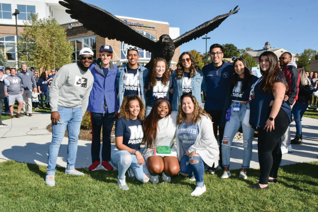 a diverse group of alumni pose in front of the Hawk Statute