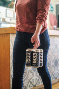 A photo of a woman from the chest down walking and holding a four pack of Bradley Brew Project's 1933 Great Hall IPA.