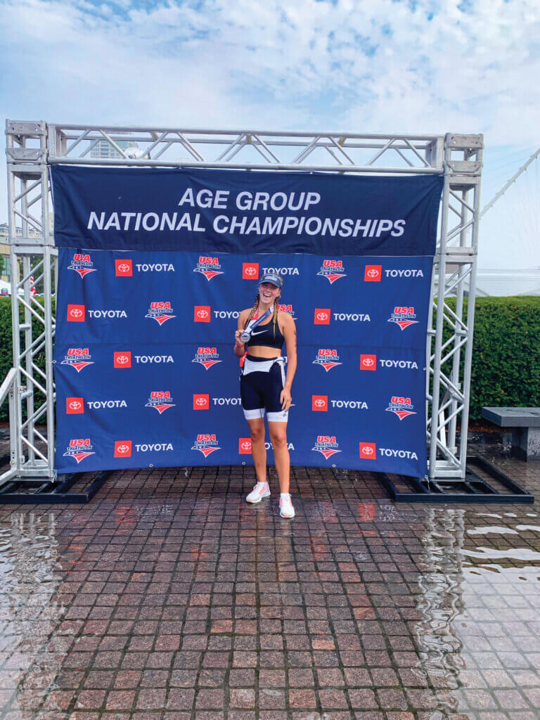 Alayna stands outside and shows off her medal after running a triathlon in 2022.