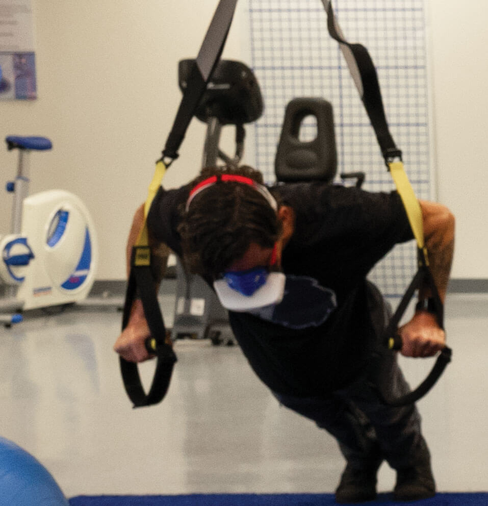 A person performs suspended push-ups while wearing a wireless oxygen uptake analyzer mask