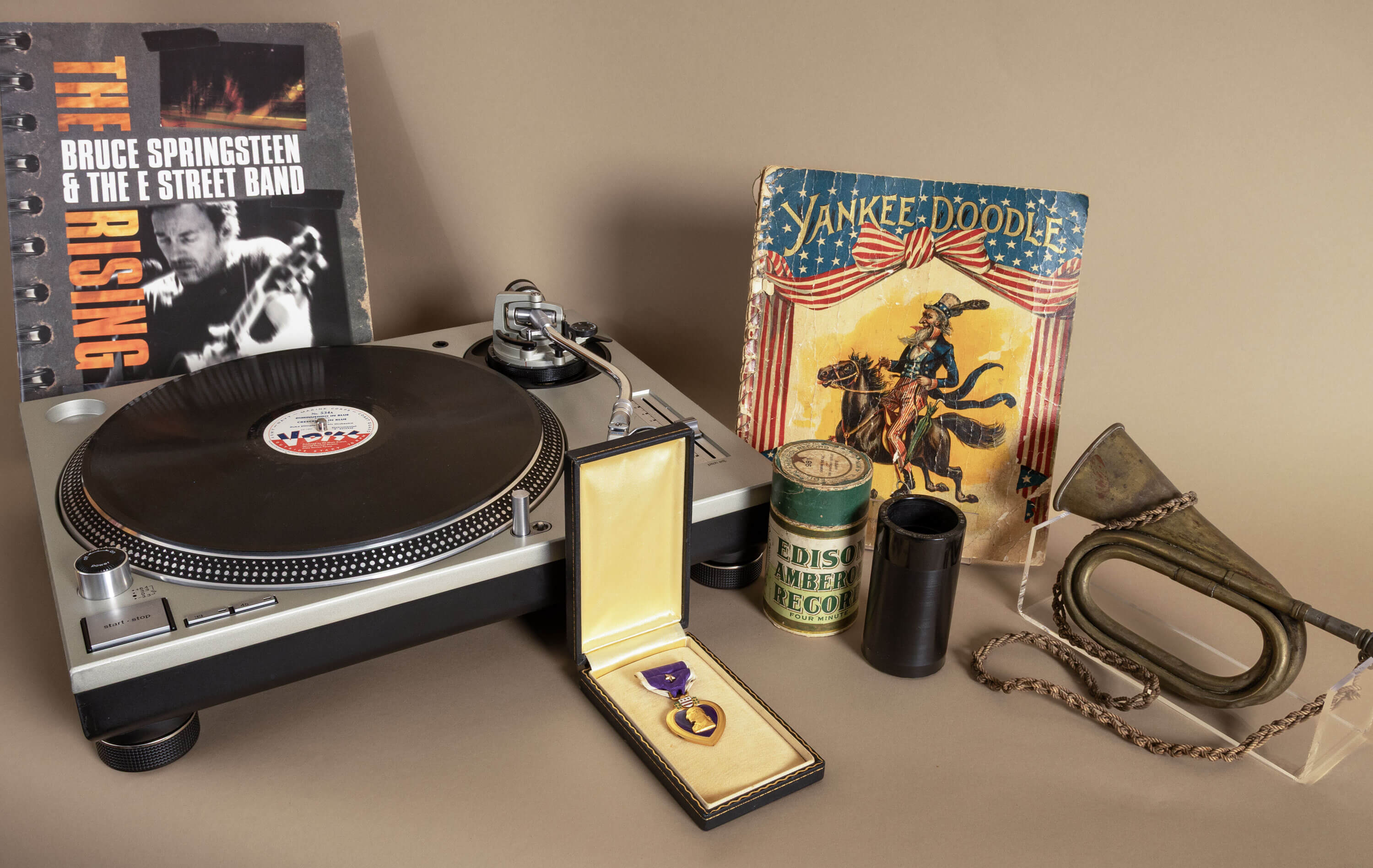 Artifacts representing American music history, including a turntable, Purple Heart medal, bugle, and a vintage "Yankee Doodle" songbook.