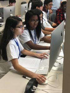 Several young girls looking at a computer while one is operating it. 