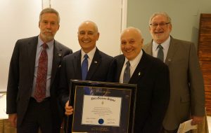 Four men posing with a award in a frame. 