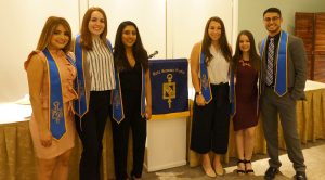 a group of six people wearing blue stoles posing next to each other with a banner in between them. 