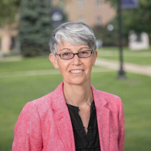 A formal photo of Belinda Andersion, she is standing outside with grass, a path, and a building in the background. 