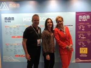 A photo of three people posing in front of a detailed background about a conference. 