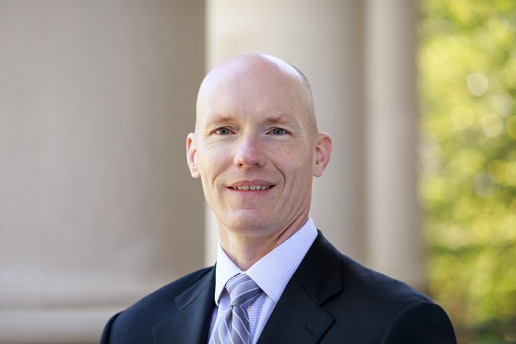 Prof. Robert Scott standing on porch of Great Hall, wearing suit and tie