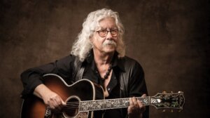 Arlo Guthrie playing guitar while seated