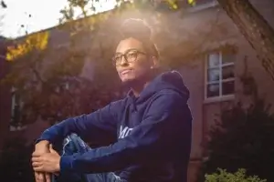 Male student sitting with hands across knees, with sunlight reflecting off a nearby building